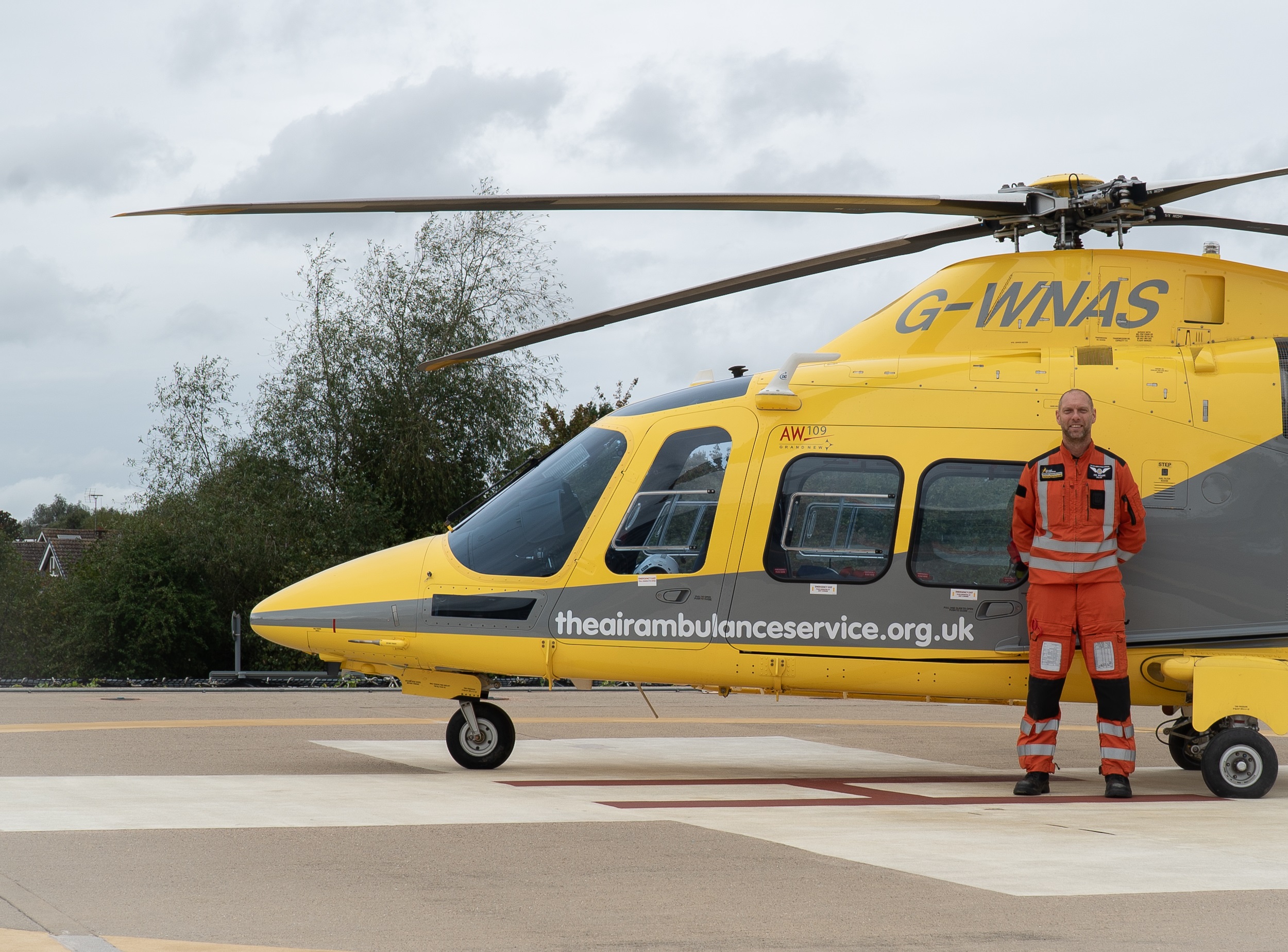 A photograph of an air ambulance paramedic in front of a yellow helicopter